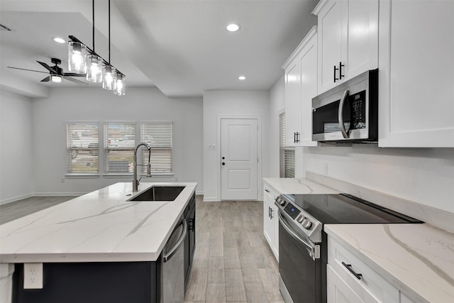 kitchen with hanging light fixtures, stainless steel appliances, a center island with sink, white cabinetry, and sink