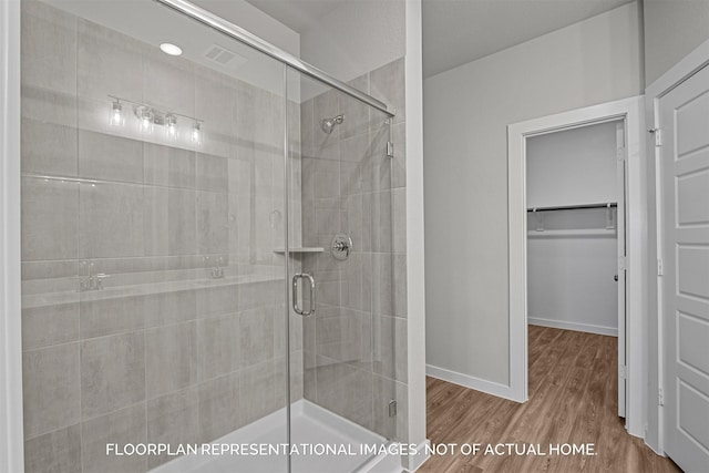 bathroom featuring a shower stall, baseboards, a walk in closet, and wood finished floors