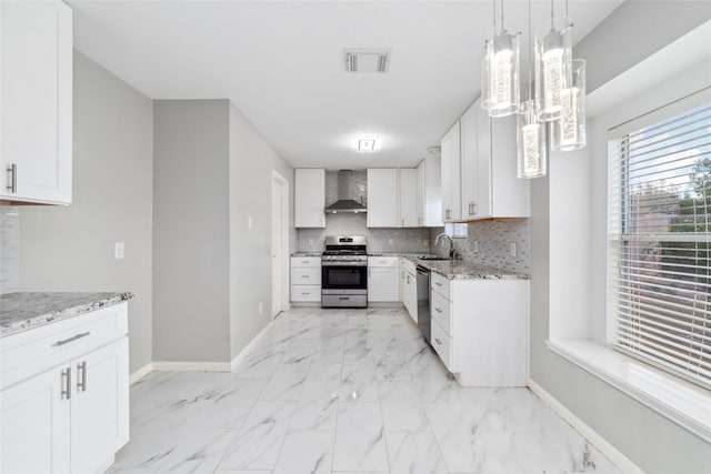 kitchen featuring decorative light fixtures, wall chimney range hood, white cabinetry, appliances with stainless steel finishes, and sink