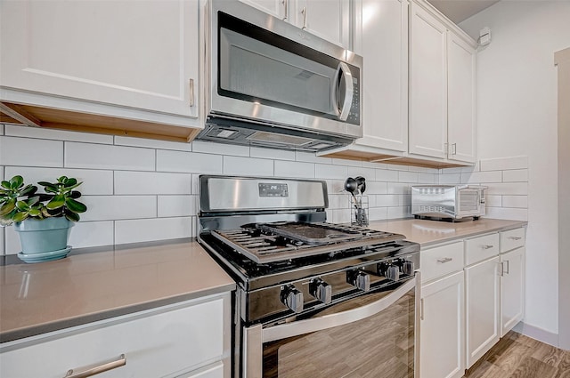 kitchen with white cabinets, stainless steel appliances, light hardwood / wood-style floors, and decorative backsplash