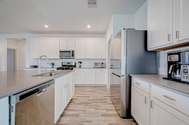 kitchen featuring stainless steel appliances, light hardwood / wood-style floors, decorative backsplash, white cabinetry, and sink