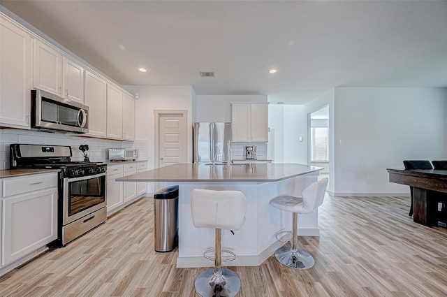 kitchen with a center island with sink, white cabinetry, light wood-type flooring, and appliances with stainless steel finishes