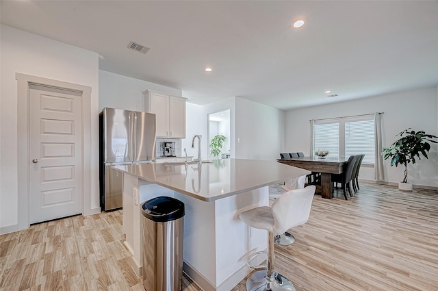 kitchen with sink, white cabinets, light hardwood / wood-style flooring, stainless steel refrigerator, and a center island with sink