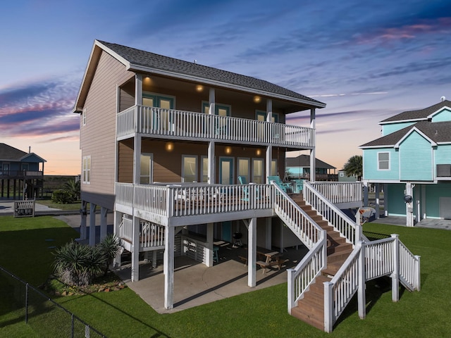 back house at dusk with a lawn, a patio area, and a balcony