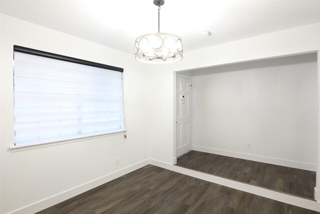 spare room with an inviting chandelier and dark hardwood / wood-style floors