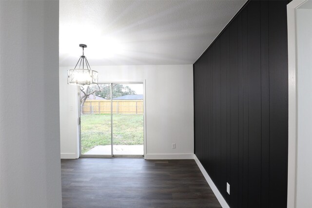 spare room with an inviting chandelier, wood walls, a wealth of natural light, and dark wood-type flooring