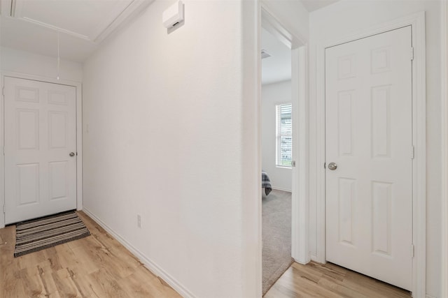 hall with light wood-style floors, attic access, and baseboards