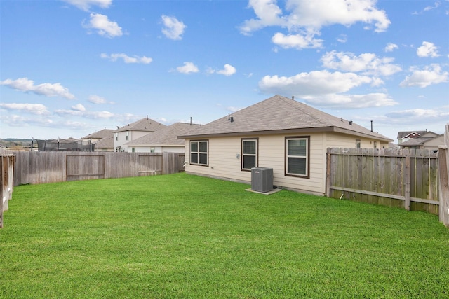 rear view of house with a shingled roof, central AC, a yard, and a fenced backyard