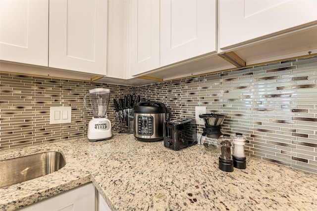 kitchen with light stone counters, white cabinetry, and decorative backsplash