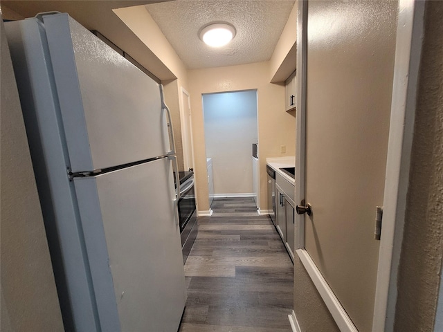 kitchen featuring a textured ceiling, stainless steel dishwasher, freestanding refrigerator, baseboards, and dark wood-style flooring