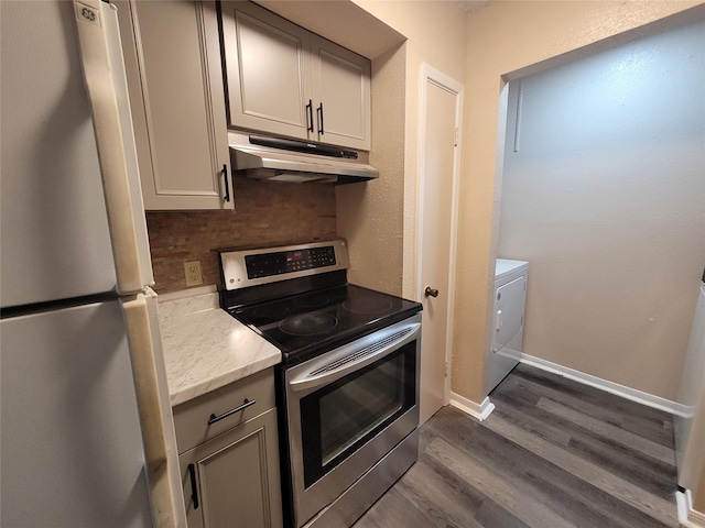 kitchen with tasteful backsplash, under cabinet range hood, stainless steel electric range, freestanding refrigerator, and washer / clothes dryer