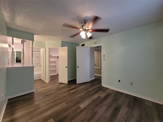 unfurnished bedroom with baseboards, a textured ceiling, a spacious closet, and dark wood-style flooring