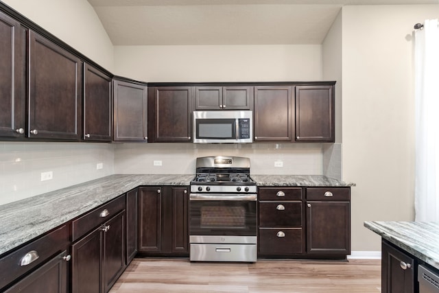 kitchen with appliances with stainless steel finishes, dark brown cabinets, light stone countertops, and tasteful backsplash