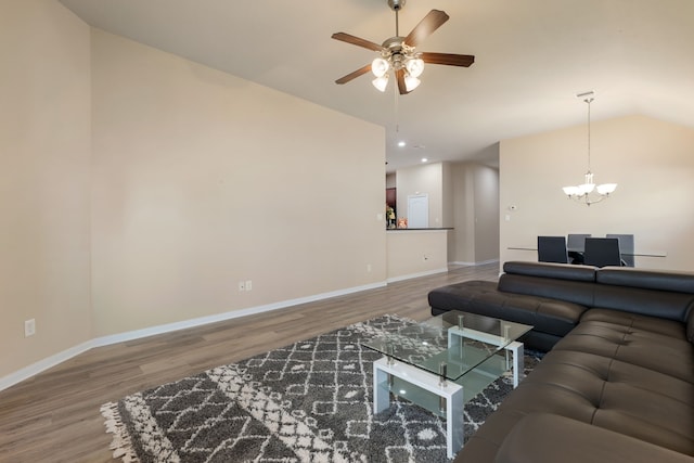 living room featuring lofted ceiling, wood-type flooring, and ceiling fan with notable chandelier