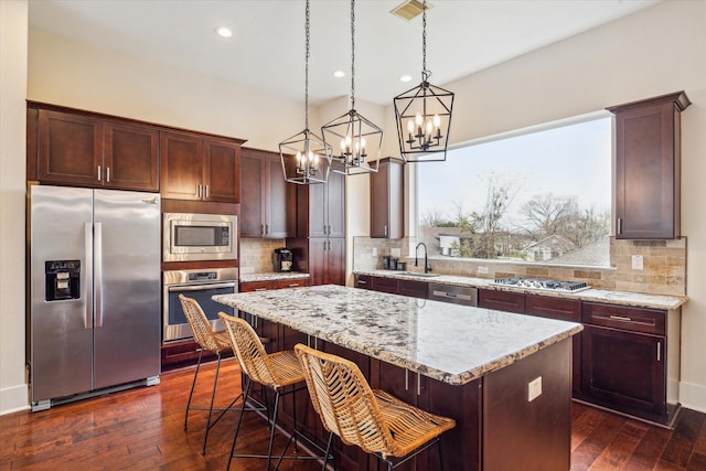 kitchen with a breakfast bar area, appliances with stainless steel finishes, hanging light fixtures, light stone counters, and a kitchen island