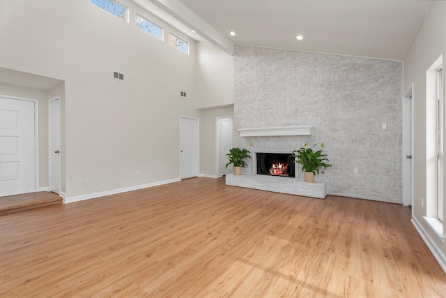 unfurnished living room featuring light hardwood / wood-style floors, a brick fireplace, high vaulted ceiling, and plenty of natural light