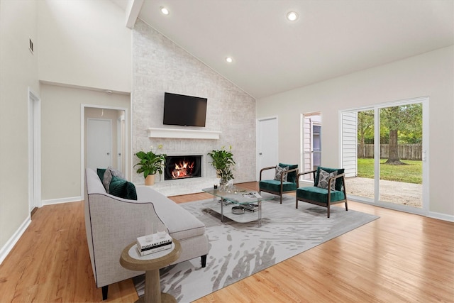 living room featuring high vaulted ceiling, a brick fireplace, and light hardwood / wood-style flooring