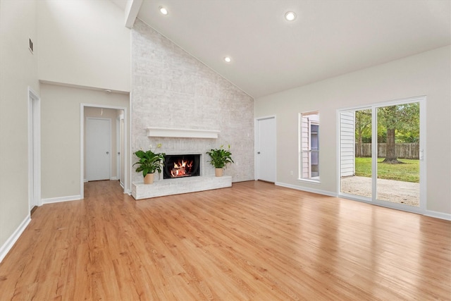 unfurnished living room featuring a fireplace, high vaulted ceiling, beam ceiling, and light hardwood / wood-style flooring