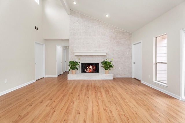 unfurnished living room featuring light wood-type flooring, a brick fireplace, and high vaulted ceiling