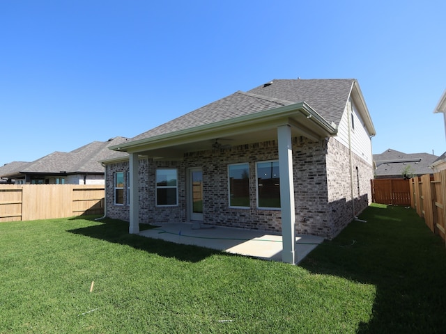 rear view of house with a lawn, brick siding, a patio area, a shingled roof, and a fenced backyard