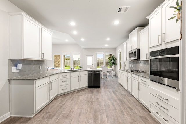 kitchen featuring stainless steel appliances, white cabinetry, light stone countertops, and kitchen peninsula