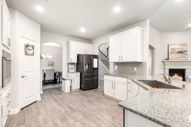 kitchen with stainless steel appliances, sink, white cabinetry, light stone counters, and light hardwood / wood-style flooring