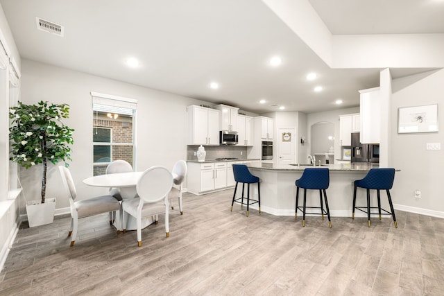 kitchen featuring stainless steel appliances, light wood-type flooring, white cabinets, and a kitchen breakfast bar