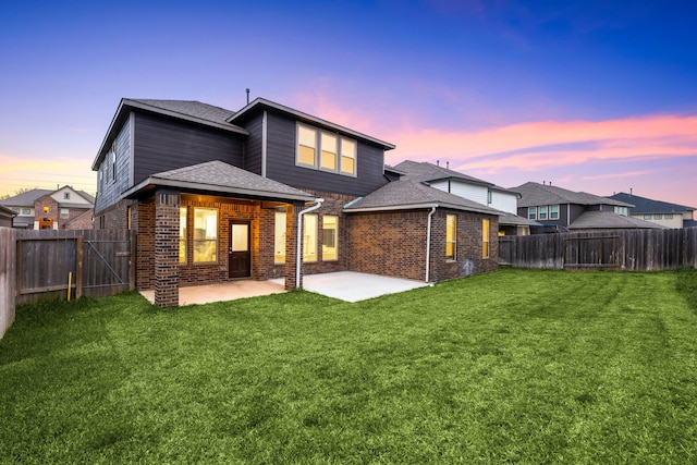 back house at dusk with a patio area and a lawn