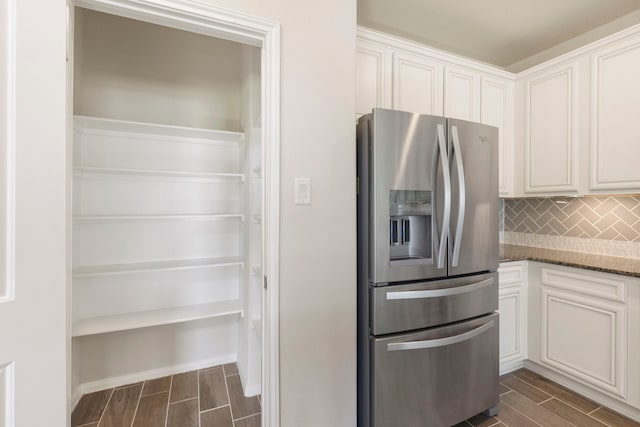 kitchen featuring white cabinetry, decorative backsplash, stainless steel fridge, and dark stone counters