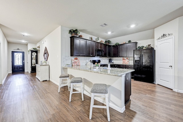 kitchen with black appliances, kitchen peninsula, light stone counters, decorative backsplash, and dark brown cabinetry