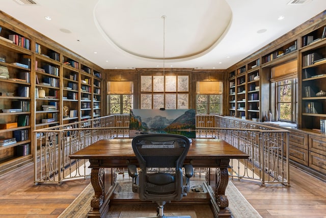 office area with wood-type flooring, a tray ceiling, and built in features