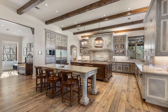 kitchen featuring built in appliances, decorative light fixtures, light wood-type flooring, tasteful backsplash, and a kitchen island