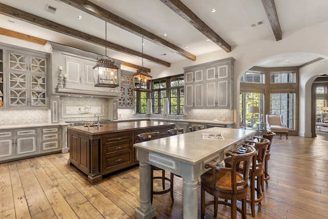 kitchen with hanging light fixtures, light hardwood / wood-style flooring, a kitchen island with sink, and tasteful backsplash