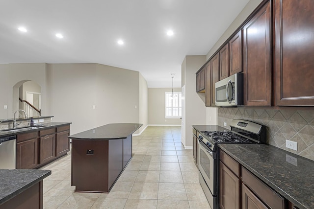 kitchen with dark stone countertops, stainless steel appliances, decorative backsplash, sink, and decorative light fixtures