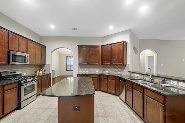 kitchen featuring dark stone countertops, appliances with stainless steel finishes, a center island, kitchen peninsula, and sink