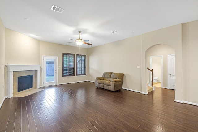 unfurnished room with a tiled fireplace, ceiling fan, and dark wood-type flooring