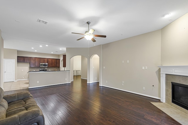 unfurnished living room featuring a tile fireplace, ceiling fan, and dark wood-type flooring