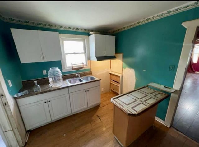 kitchen with white cabinets, light wood-type flooring, a kitchen island, and sink