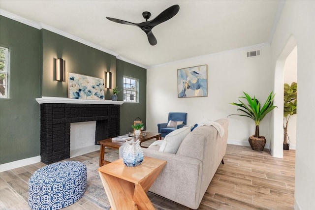 living room with a fireplace, ceiling fan, crown molding, and light hardwood / wood-style flooring