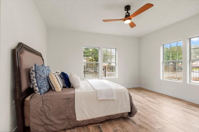 bedroom featuring ceiling fan, light hardwood / wood-style floors, and multiple windows