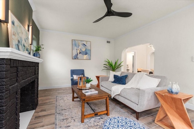 living room featuring ornamental molding, ceiling fan, a stone fireplace, and wood-type flooring