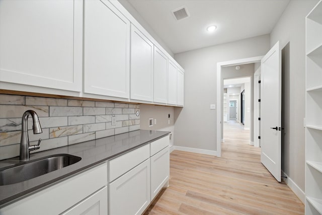 kitchen with decorative backsplash, light hardwood / wood-style floors, white cabinets, and sink