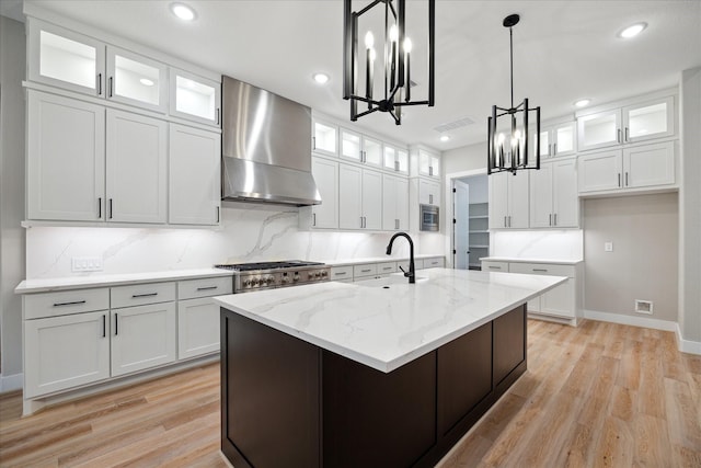 kitchen with white cabinetry, sink, wall chimney range hood, and a kitchen island with sink