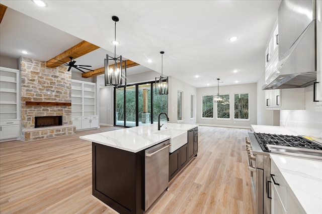 kitchen with a center island with sink, appliances with stainless steel finishes, sink, wall chimney exhaust hood, and beamed ceiling