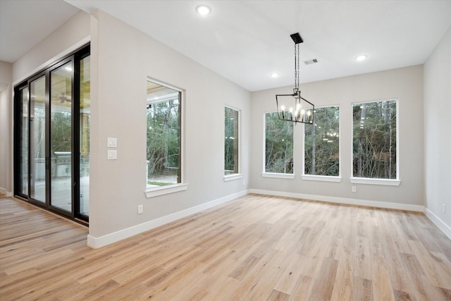 unfurnished dining area with a wealth of natural light, light hardwood / wood-style flooring, and a notable chandelier