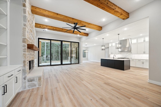 unfurnished living room with ceiling fan, light hardwood / wood-style floors, a fireplace, and beam ceiling