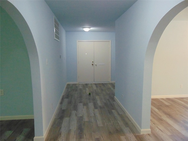 hall featuring visible vents, wood finished floors, arched walkways, and baseboards