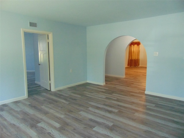 spare room featuring arched walkways, visible vents, baseboards, and wood finished floors