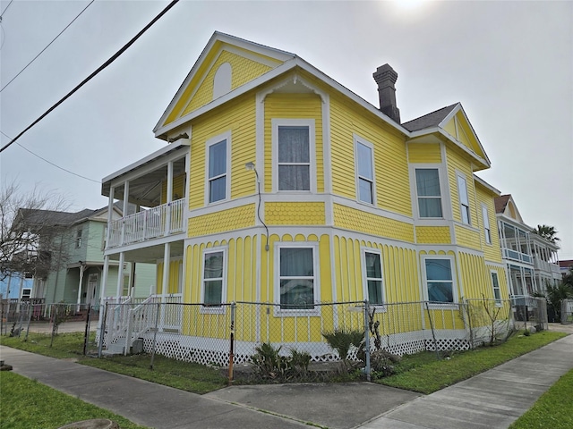 view of side of property featuring a fenced front yard, covered porch, board and batten siding, and a balcony