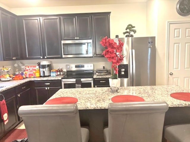 kitchen featuring stainless steel appliances, a breakfast bar, and light stone countertops